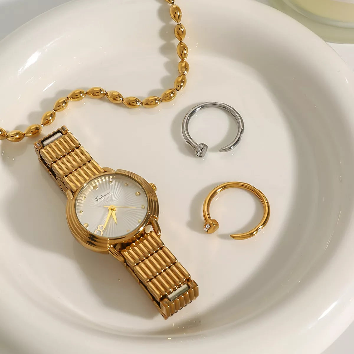 Stainless steel zircon open ring displayed with gold watch and bracelet on white plate