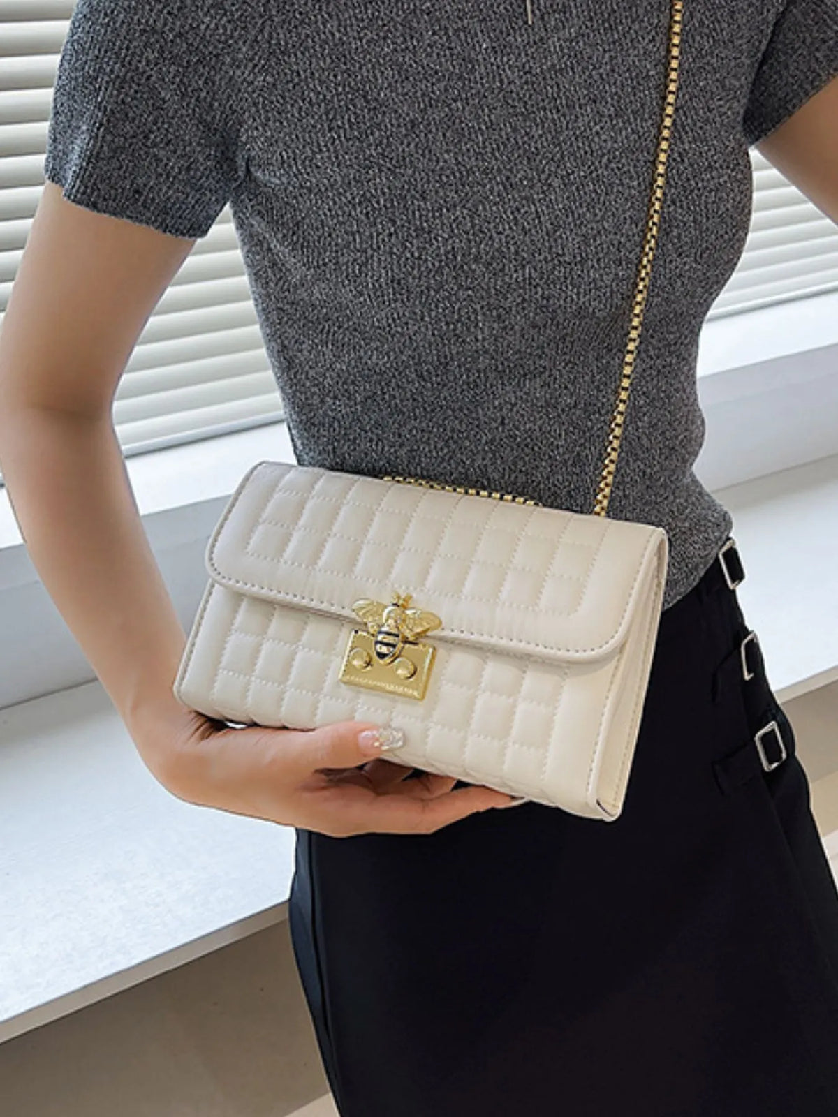 Small white quilted chain shoulder bag in PU leather with gold clasp and chain strap worn by a person