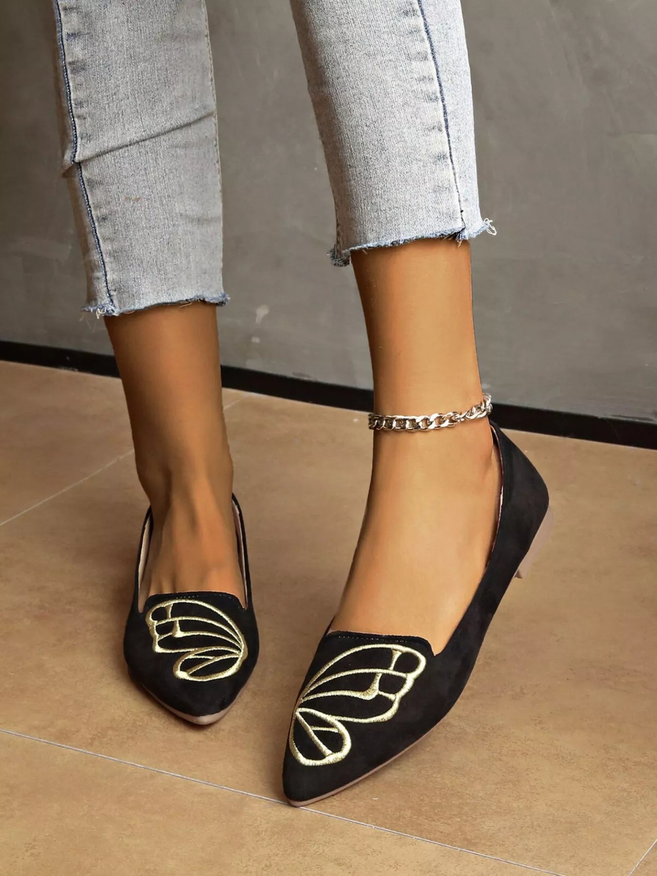 Black point toe slip-on flats with gold embroidery, worn with light blue denim jeans
