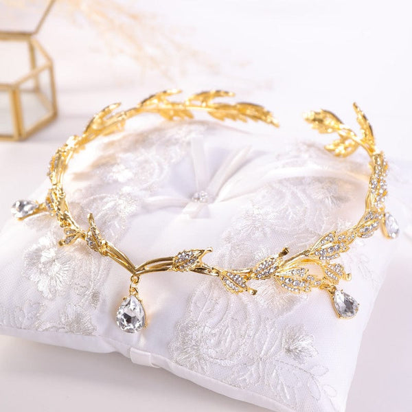 Golden crown headband with drop-shaped diamonds on a white cushion.