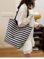 Large striped canvas tote bag with navy and white horizontal stripes and long handles.