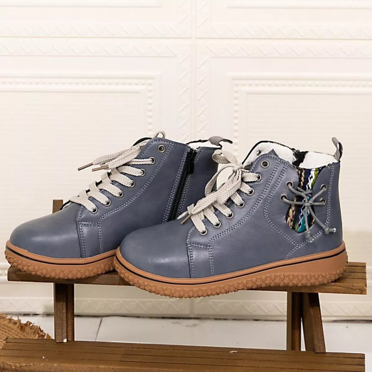 Blue round toe platform ankle boots with beige laces and rubber soles on wooden bench