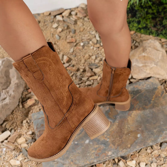 Brown suede block heel western boots with mid heel and side zipper on rocky surface