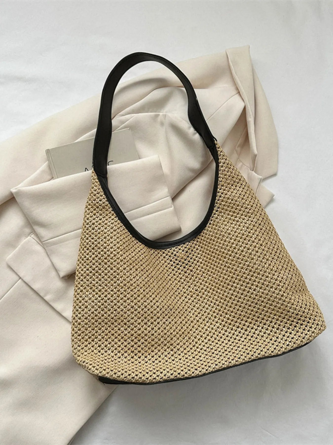 Medium woven straw shoulder bag with black PU leather handle on white fabric background