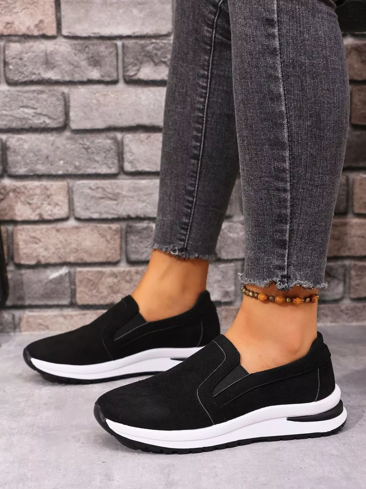 Black slip-on sneakers with white contrast sole worn with grey jeans