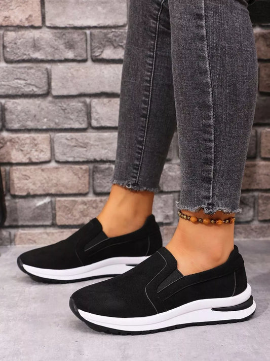 Black slip-on sneakers with white contrast sole worn with grey jeans