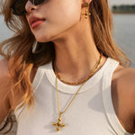 Woman wearing 18K gold-plated tiger's eye cross pendant necklace with gold earrings and white tank top outdoors