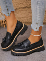 Black tassel round toe platform loafers with mid heels and rugged rubber soles on feet in blue jeans