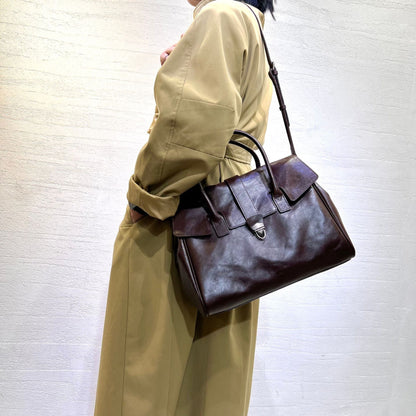 Vintage brown genuine leather bag with a medium hardness, worn by a woman.