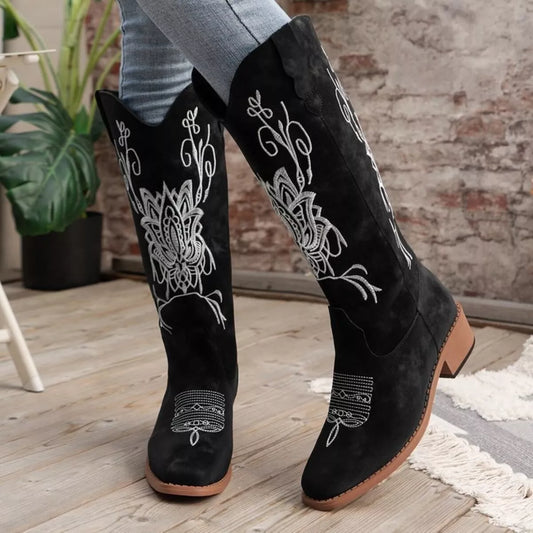 Black embroidered block heel boots with white floral design, mid heel, and tan sole worn with jeans