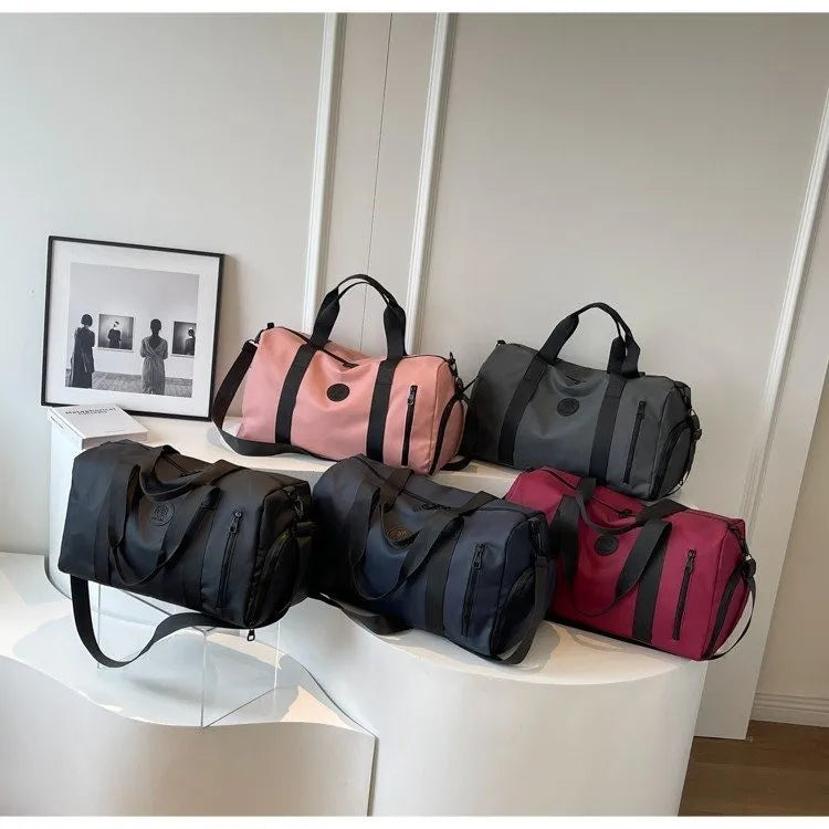 Five large Oxford cloth travel bags in black, navy, gray, pink, and red with handles and shoulder straps displayed indoors