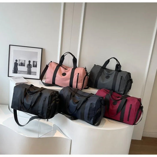 Five large Oxford cloth travel bags in black, navy, gray, pink, and red with handles and shoulder straps displayed indoors