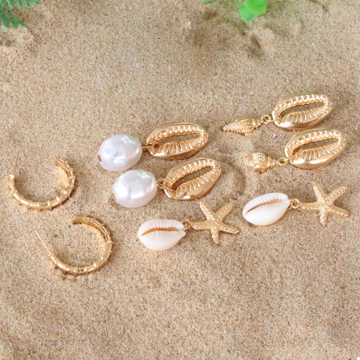 4 pair 18K gold-plated shell earrings set with freshwater pearls and starfish designs on sand background