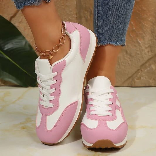 Pink and white contrast lace up round toe sneakers on feet with jeans