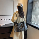 Woman carrying large gray Oxford cloth travel handbag with black straps over shoulder indoors