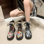 Pair of graffiti print combat boots with colorful street art design and black laces worn by person sitting on floor