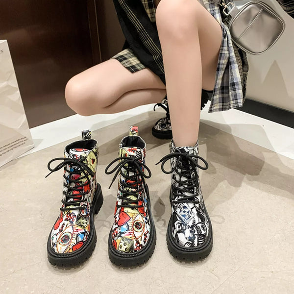 Pair of graffiti print combat boots with colorful street art design and black laces worn by person sitting on floor